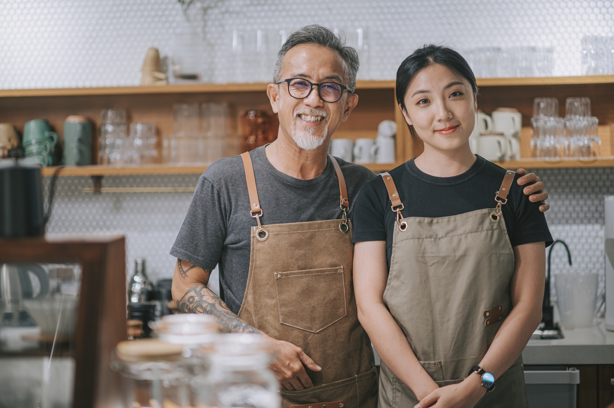 Cafe owners looking at camera smiling at coffee shop counter
