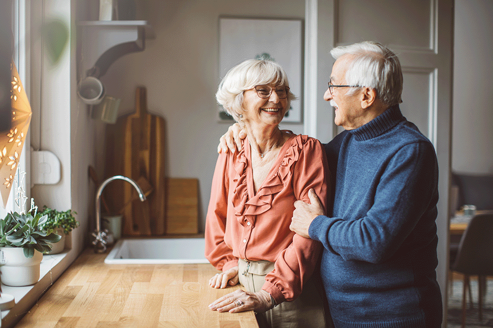 Old couple at kitchen counter smiling at each other