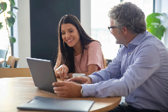 Young adult woman sitting at a laptop with her dad. Both are smiling
