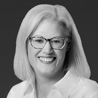 Sara McCullough headshot. She is wearing a light coloured shirt and has blond hair and glasses. She is smiling warmly at the camera. Photo is in black and while